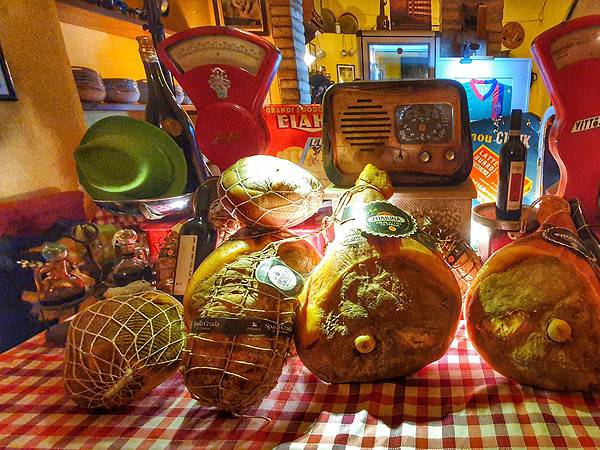 Esposizione di prosciutti e salumi tipici di Parma alla Trattoria Correri, con bilance e atmosfera rustica.