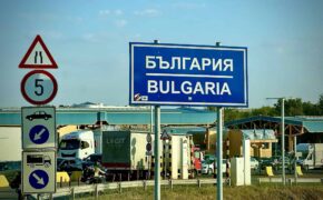 Cartello di confine Bulgaria con scritta in cirillico e traffico di auto e camion al valico di frontiera