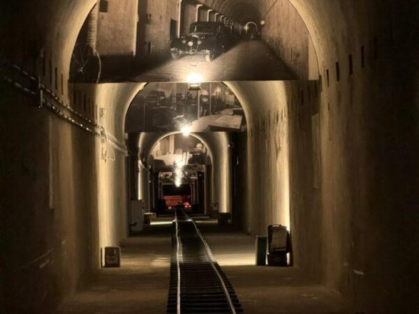 Prospettiva centrale dei binari a scartamento ridotto Decauville che si addentrano nel tunnel illuminato del bunker.