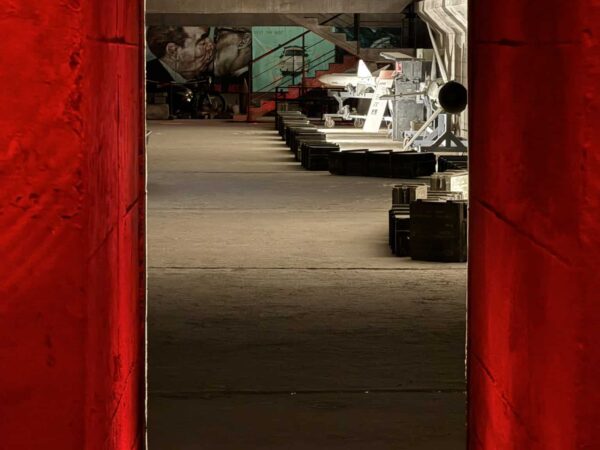 Veduta interna di una galleria con missili storici e murales del bacio tra Brežnev e Honecker incorniciata da pilastri rossi.